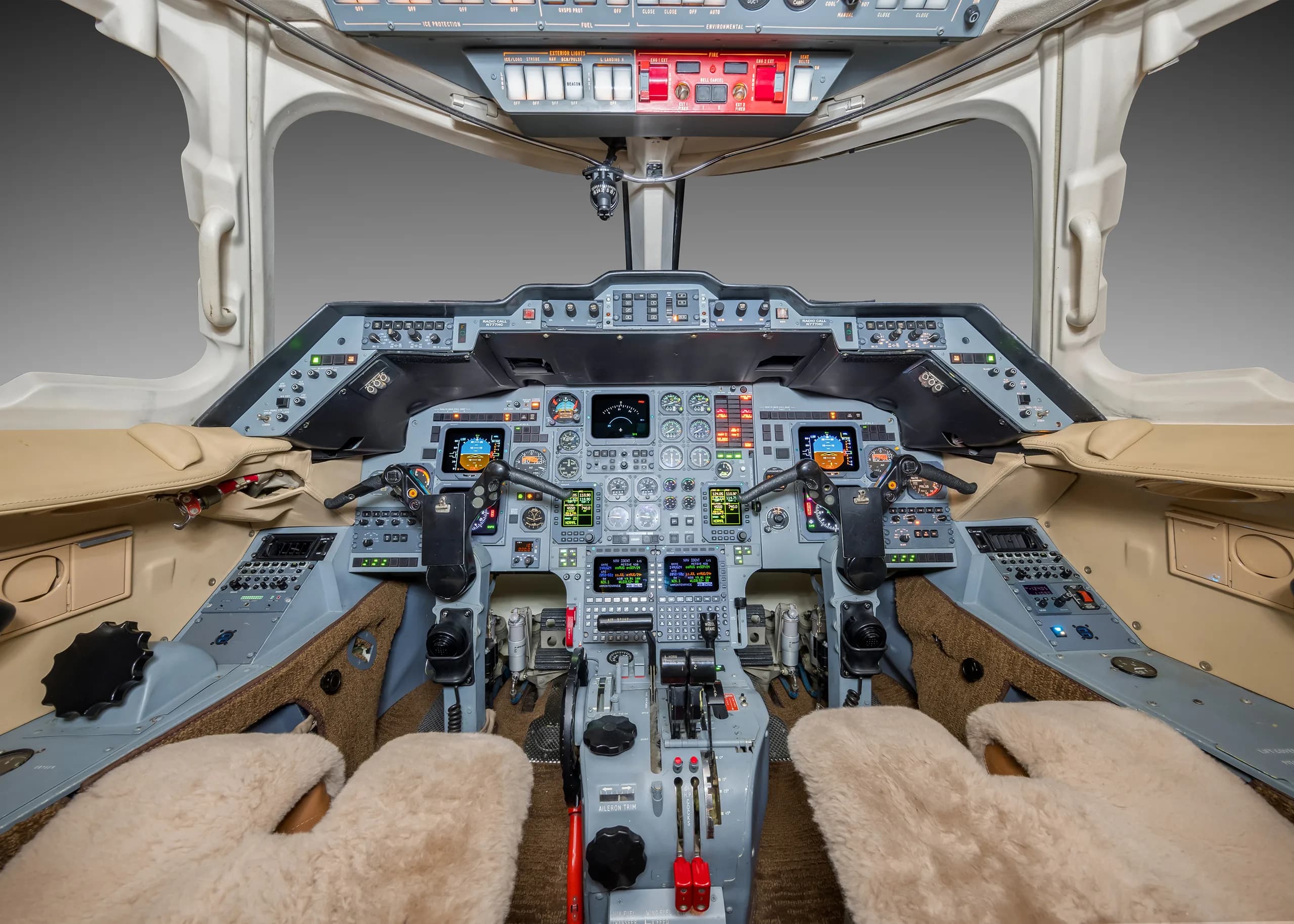 The cockpit of a business jet with multiple screens, instruments, and tan sheepskin seat covers.