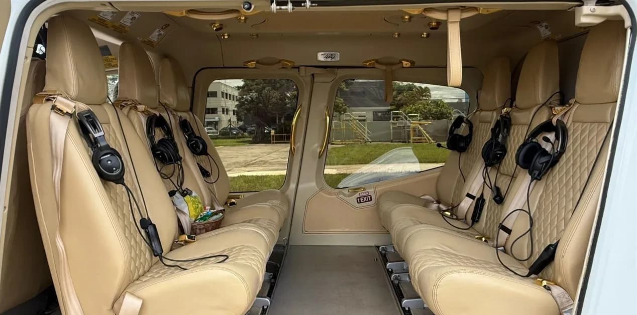 The luxurious tan leather interior of a helicopter cabin with multiple headsets on the seats.