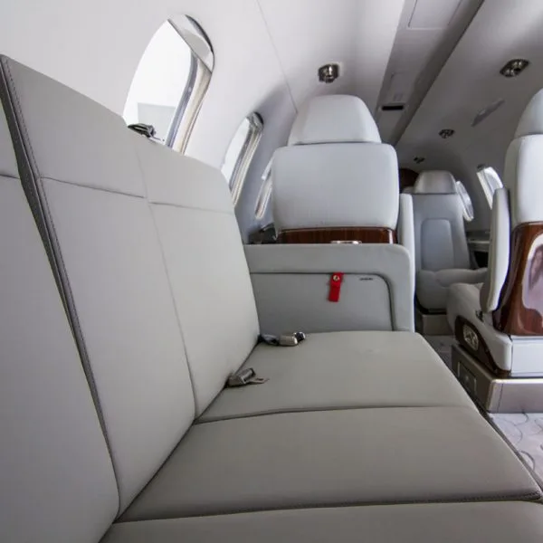 A close-up view of a light grey leather bench seat in the private jet's cabin.