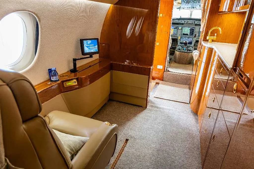 The private jet's forward cabin area with a small counter, a single seat, and a glimpse of the cockpit.