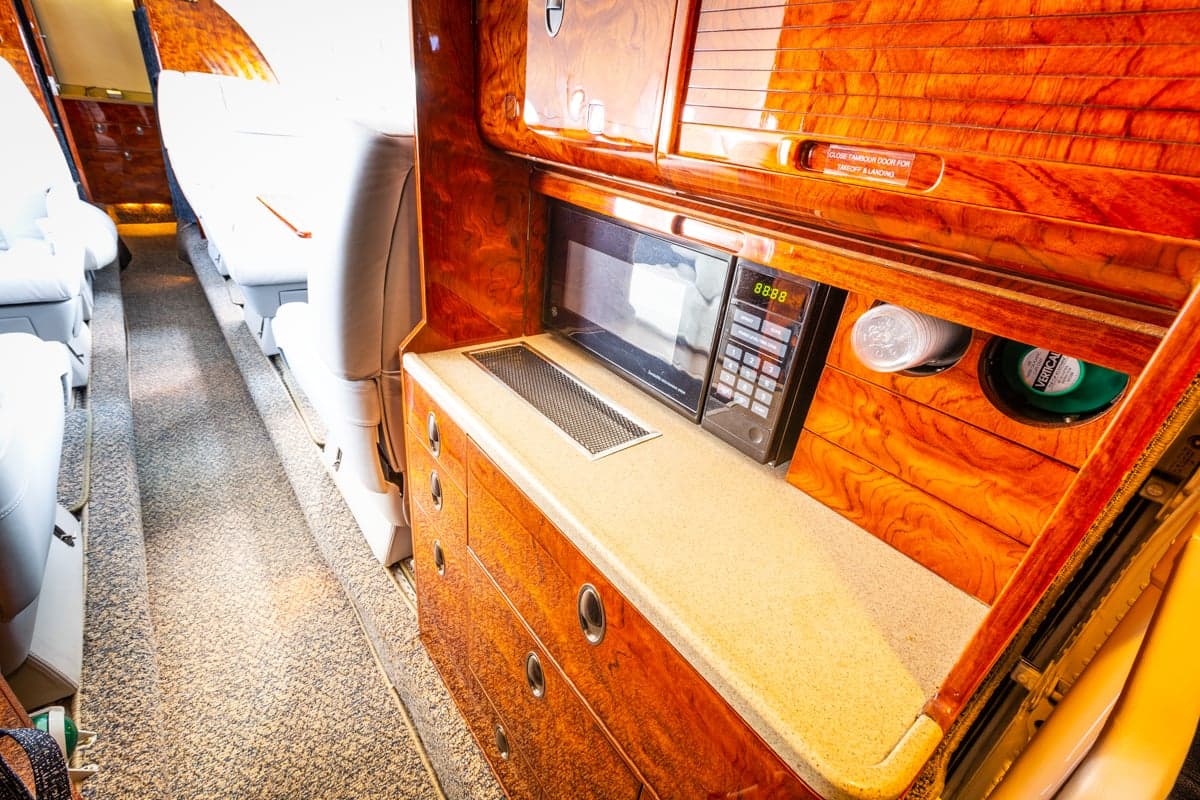 A view of the galley area inside the aircraft cabin, featuring wood cabinetry and a microwave.