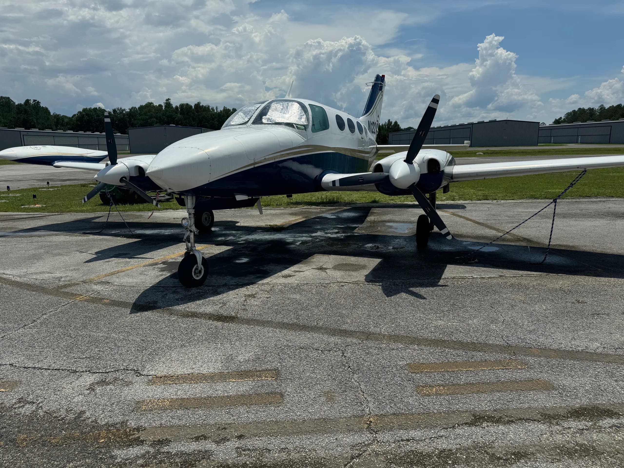 Front view of a white and blue Cessna 401 (or similar twin-engine prop) aircraft, registration N122AT, parked on an asphalt ramp.