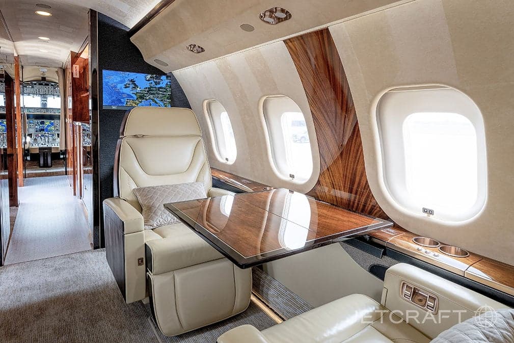 View of the aircraft cabin with a tan leather seat and wood trim, with a table extended.
