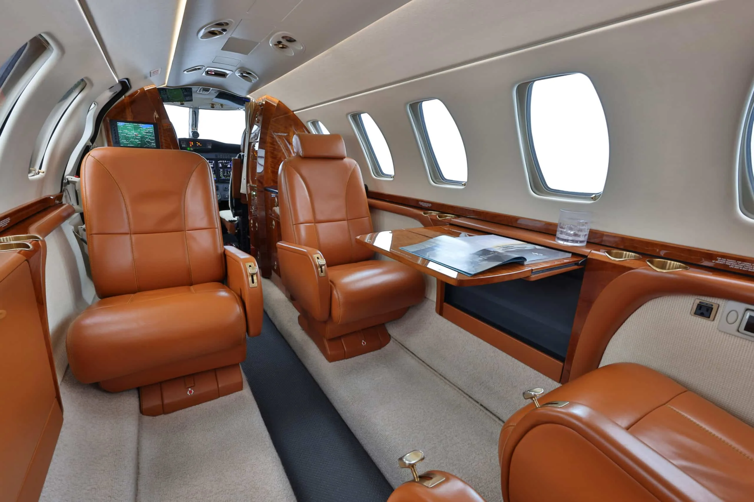 Interior view of a private jet cabin with tan leather seats and a deployed wooden table.