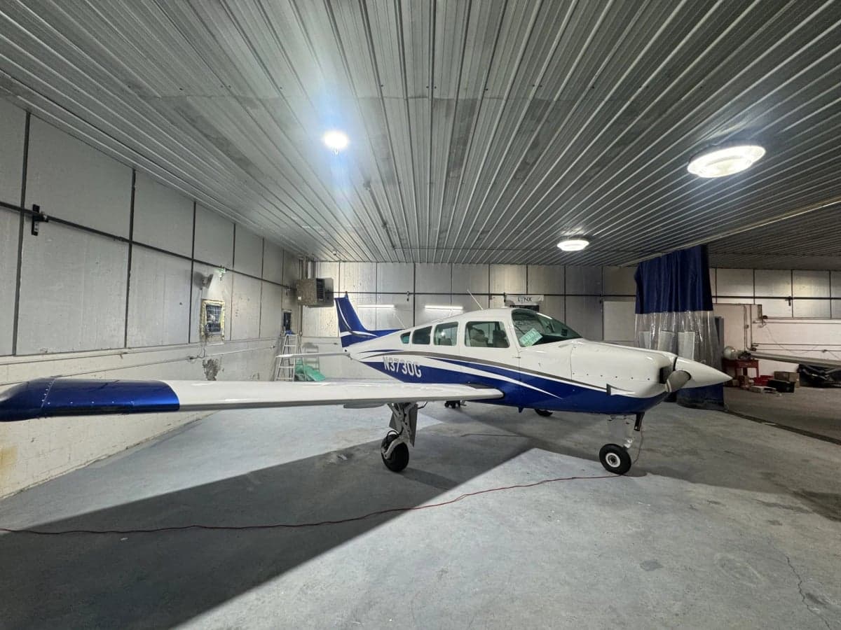 A white and blue single-engine aircraft, N3730G, viewed from the side inside a hangar.