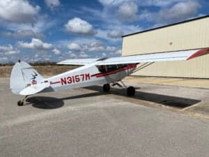 Piper Cub aircraft with red and white paint scheme parked on the tarmac.