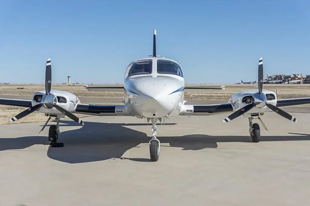 A head-on view of a white twin-engine Cessna 414 Chancellor aircraft with blue stripes on an airfield.