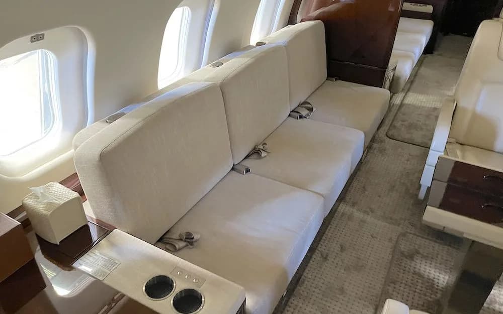 A close-up view of a cream-colored three-seat sofa in a private jet cabin next to a window.
