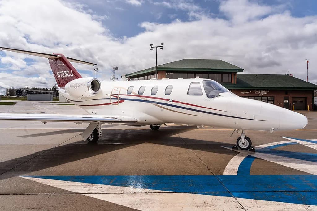 A white Cessna Citation CJ1 private jet with red and blue stripes on the fuselage, parked on an airport tarmac.