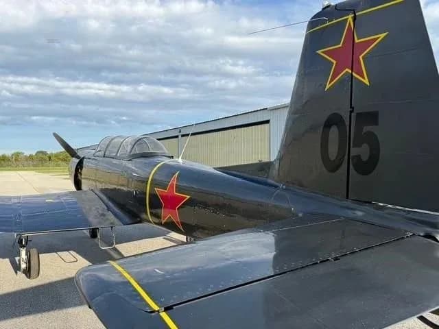 A close-up view of the tail and rear fuselage of a dark gray Yak-52 aircraft, showing a red star and '05' on the tail.