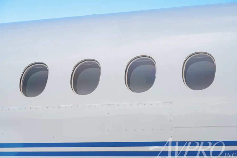 A close-up view of four oval cabin windows on the white fuselage of the Dassault Falcon 900EX, N917JF.