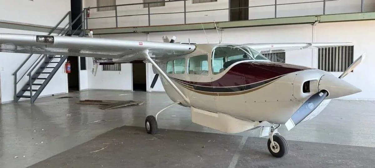 Side view of a white and maroon single-engine propeller aircraft with the propeller removed, parked in a hangar.