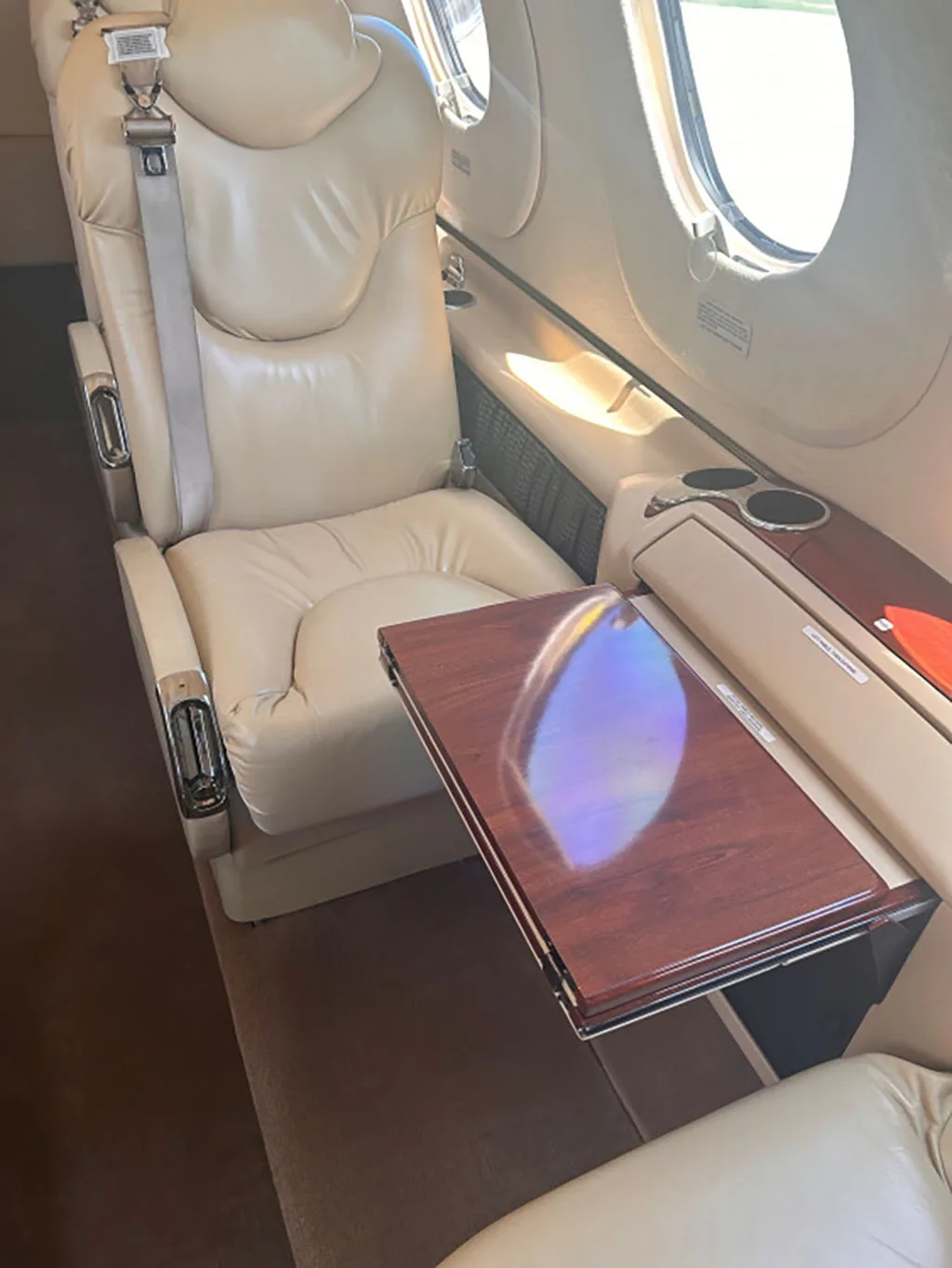 A close-up view of a light tan leather seat and a wooden fold-out table in a private jet cabin.