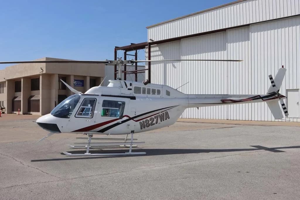 Side view of a white Bell 206 helicopter with N827WA registration, parked on an airfield.