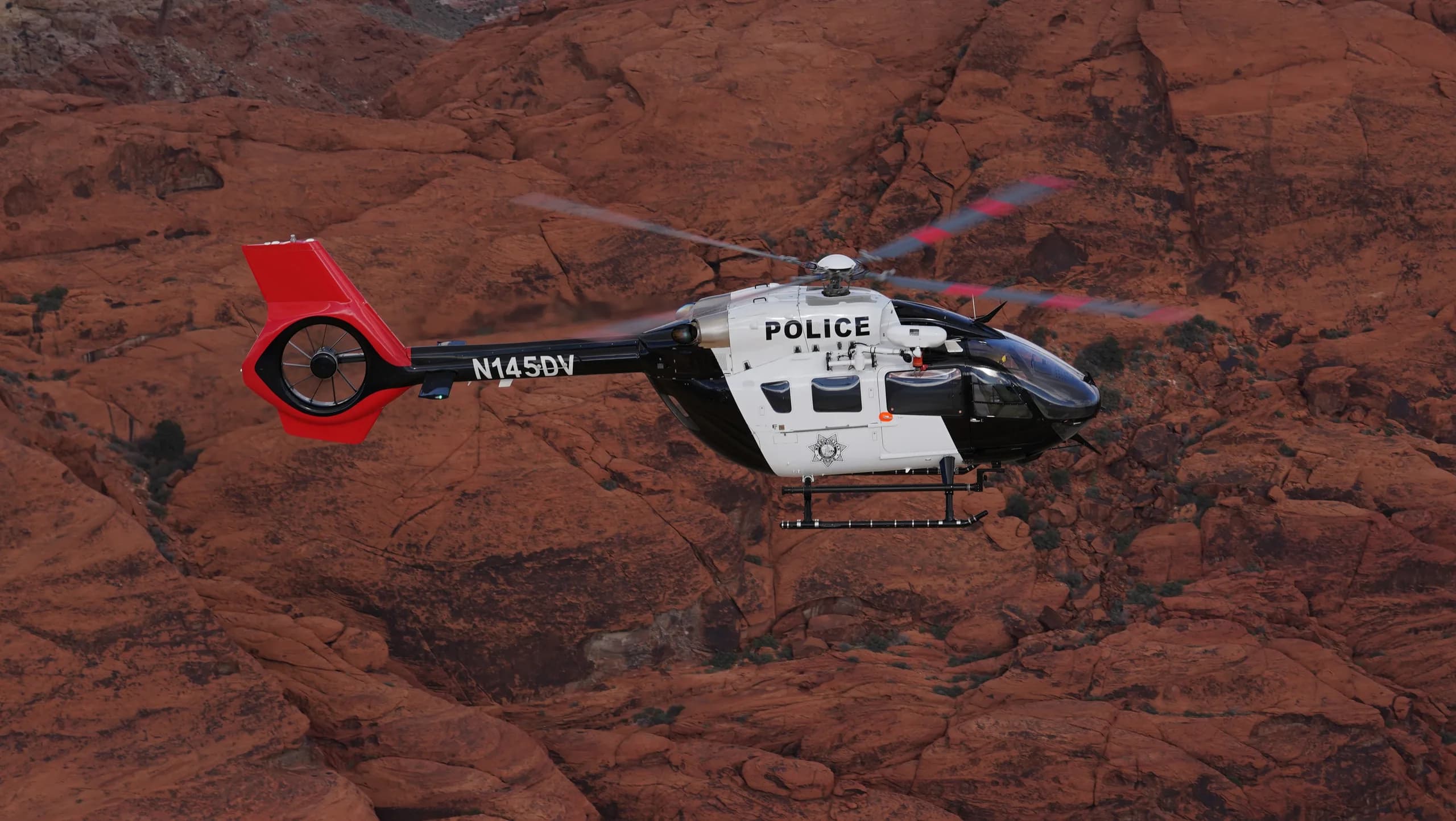 A black and white police helicopter flying over a rocky landscape.