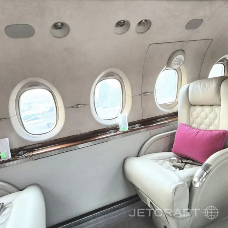 Another view of the interior cabin of a business jet, showing cream-colored seats with pink pillows and oval windows.