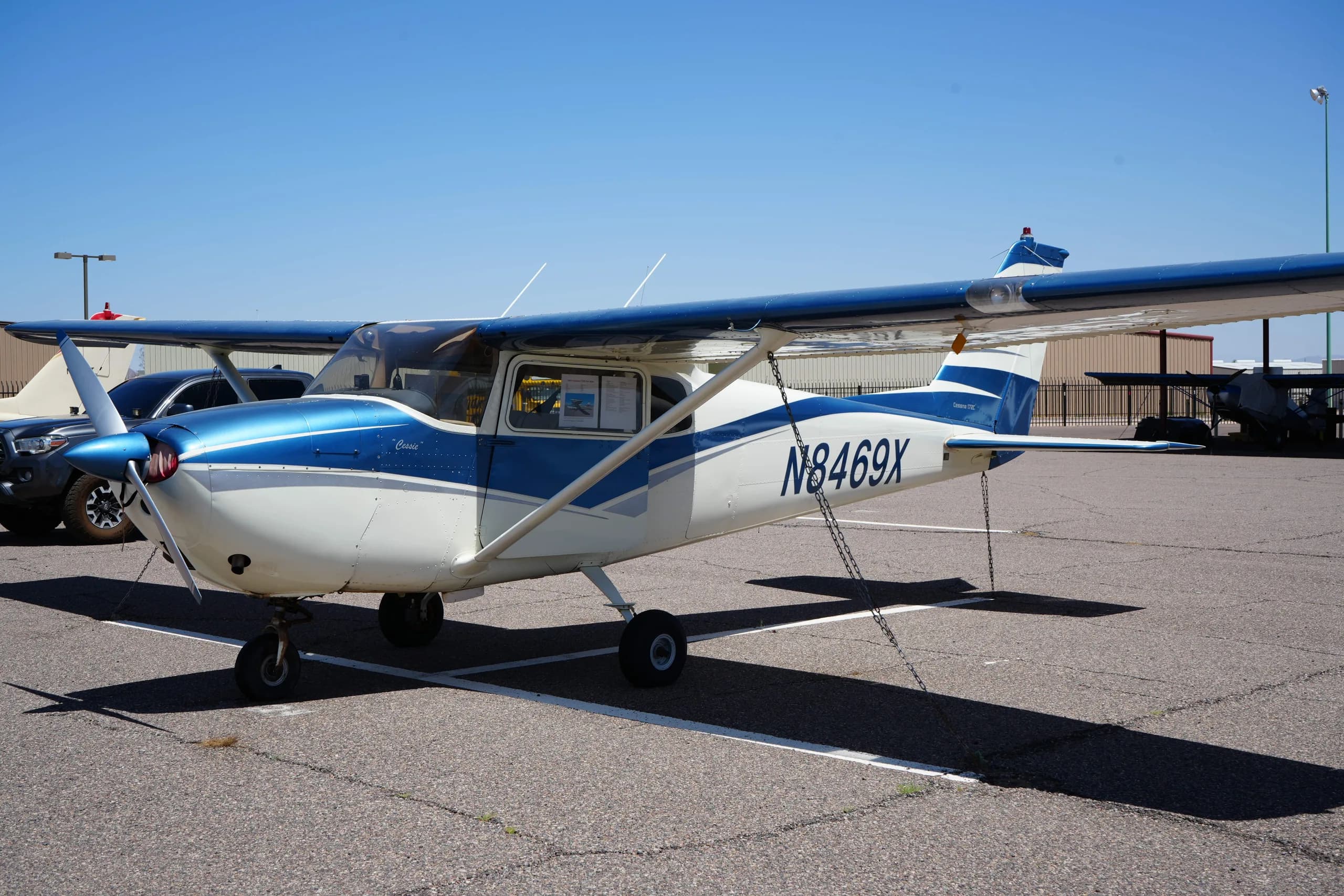 Close-up side view of a white and blue Cessna 172 (N8469X) on an airfield, showing the registration number.