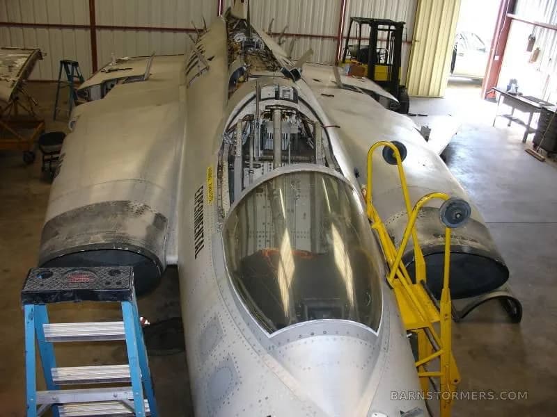 A close-up view of the front fuselage and open cockpit of a disassembled Saab Draken aircraft in a hangar.