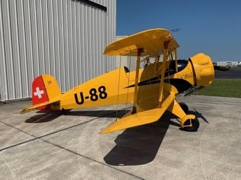 A yellow biplane with Swiss markings parked on the tarmac.