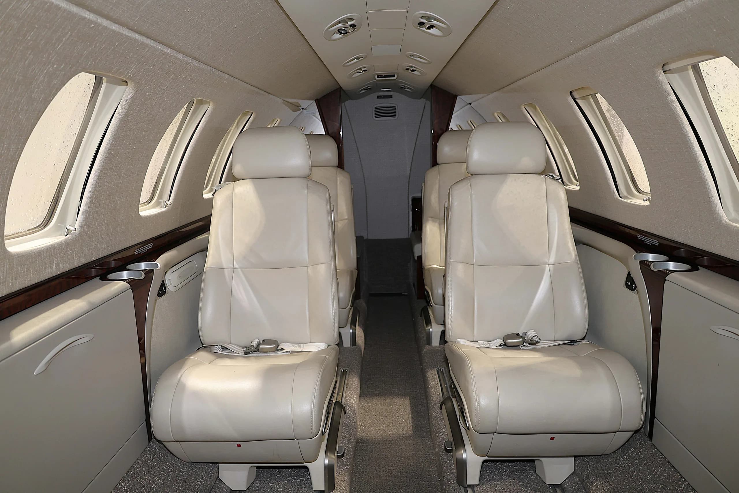 The interior cabin of a business jet with light beige leather seats arranged in a club configuration, looking towards the rear.