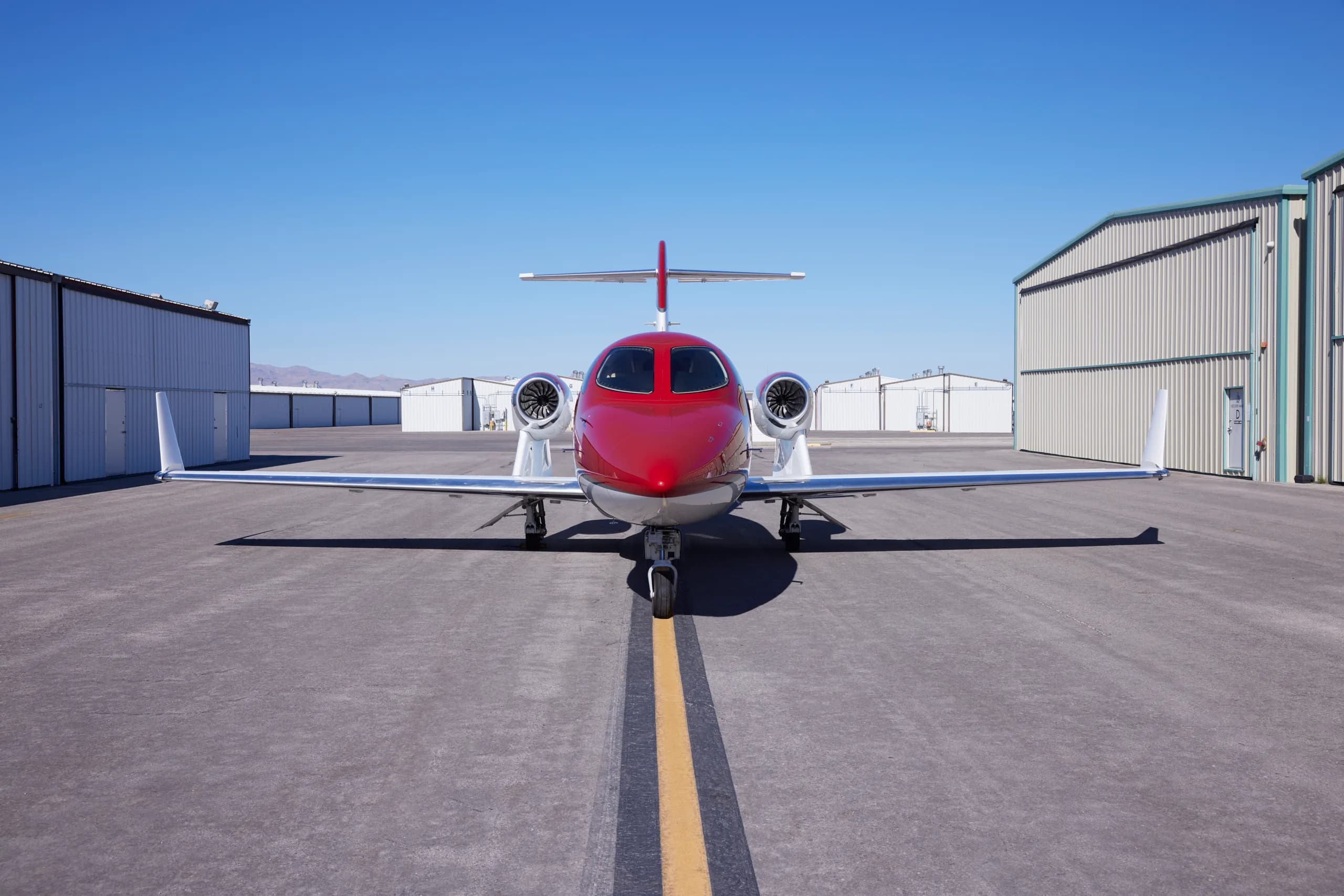 A red and white HondaJet N524HJ parked head-on on an airport tarmac with hangars in the background.