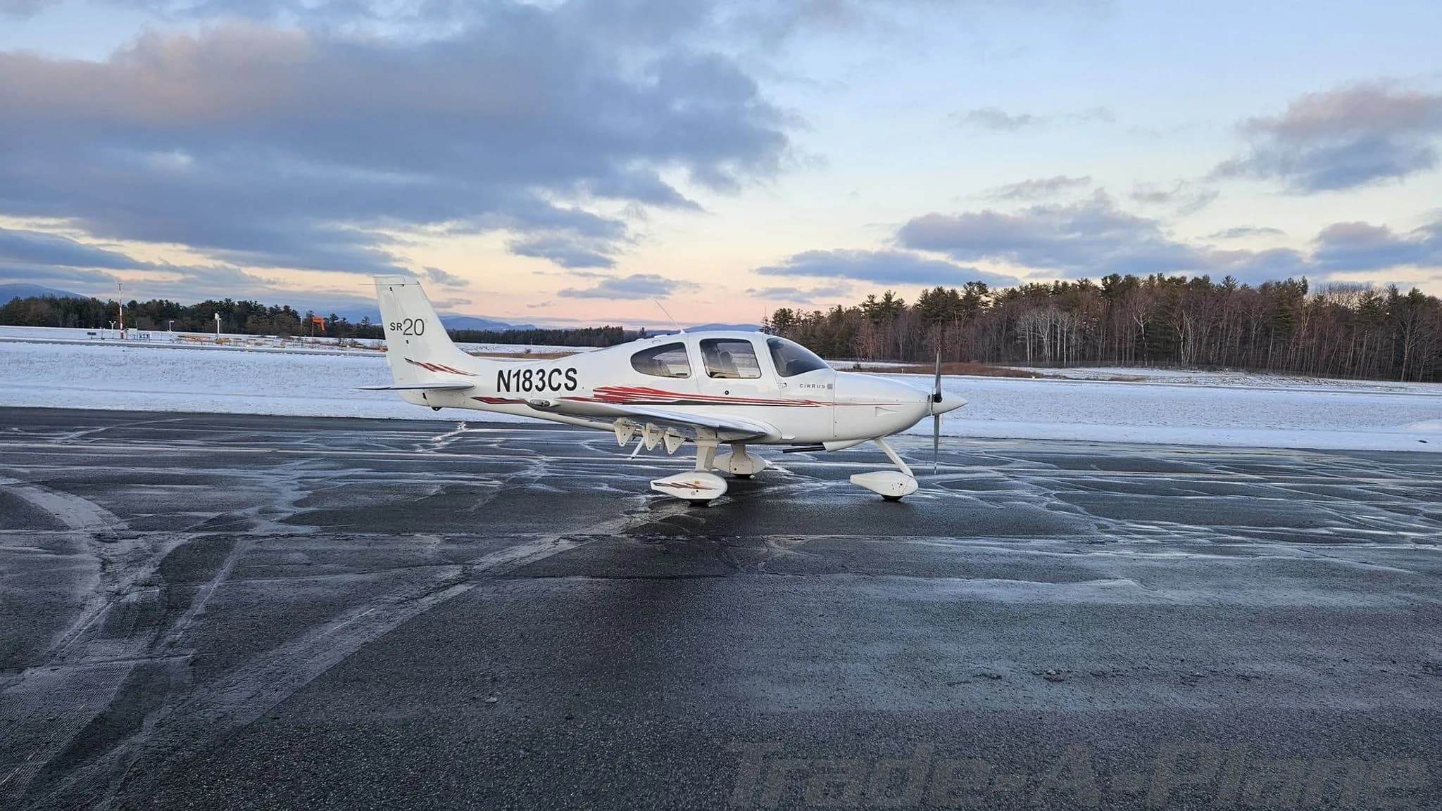 Side view of a white Cirrus SR20 aircraft with red and black stripes on a wet tarmac.