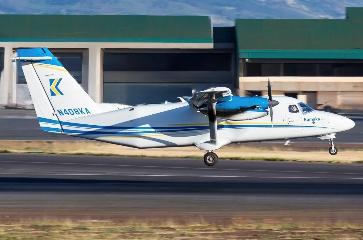 A white and blue Cessna Caravan floatplane taking off from a lake with a castle in the background.