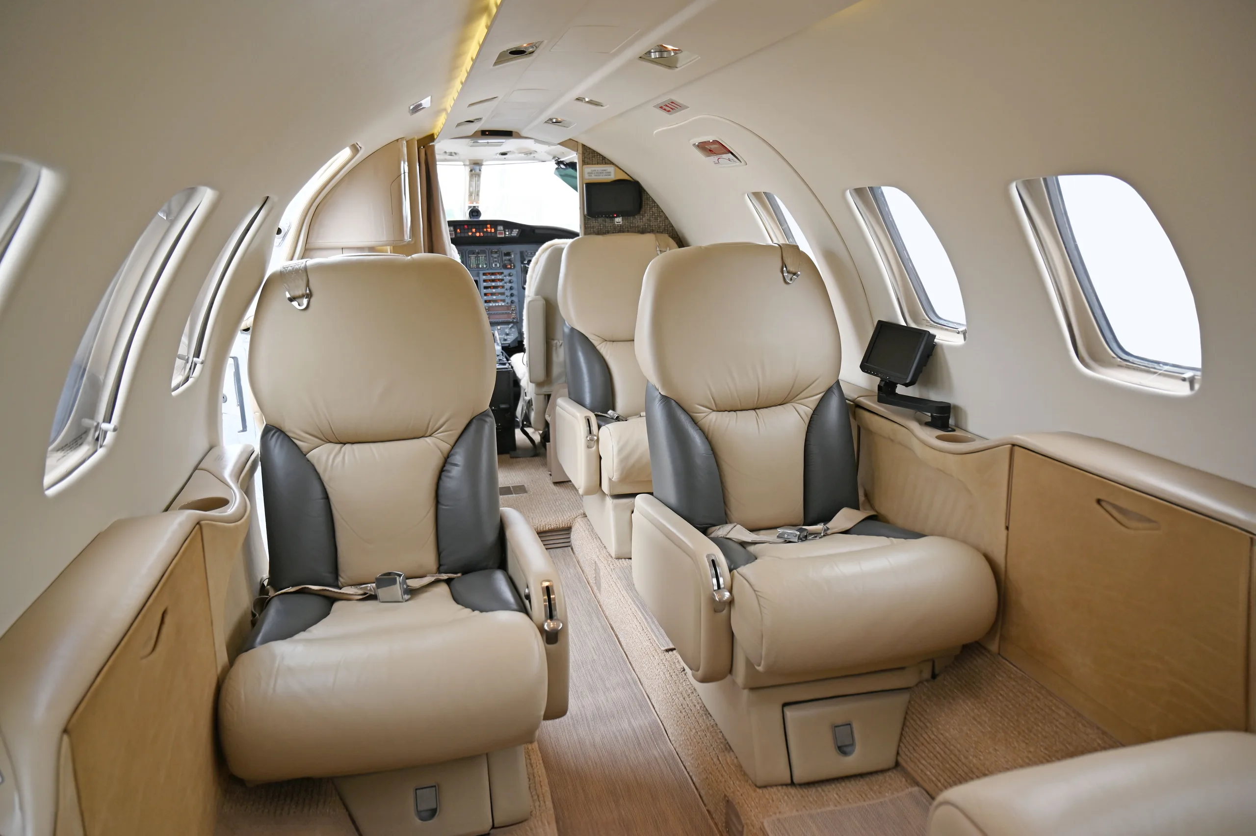 The interior cabin of a private jet, showing beige and gray leather seats and a view towards the cockpit.