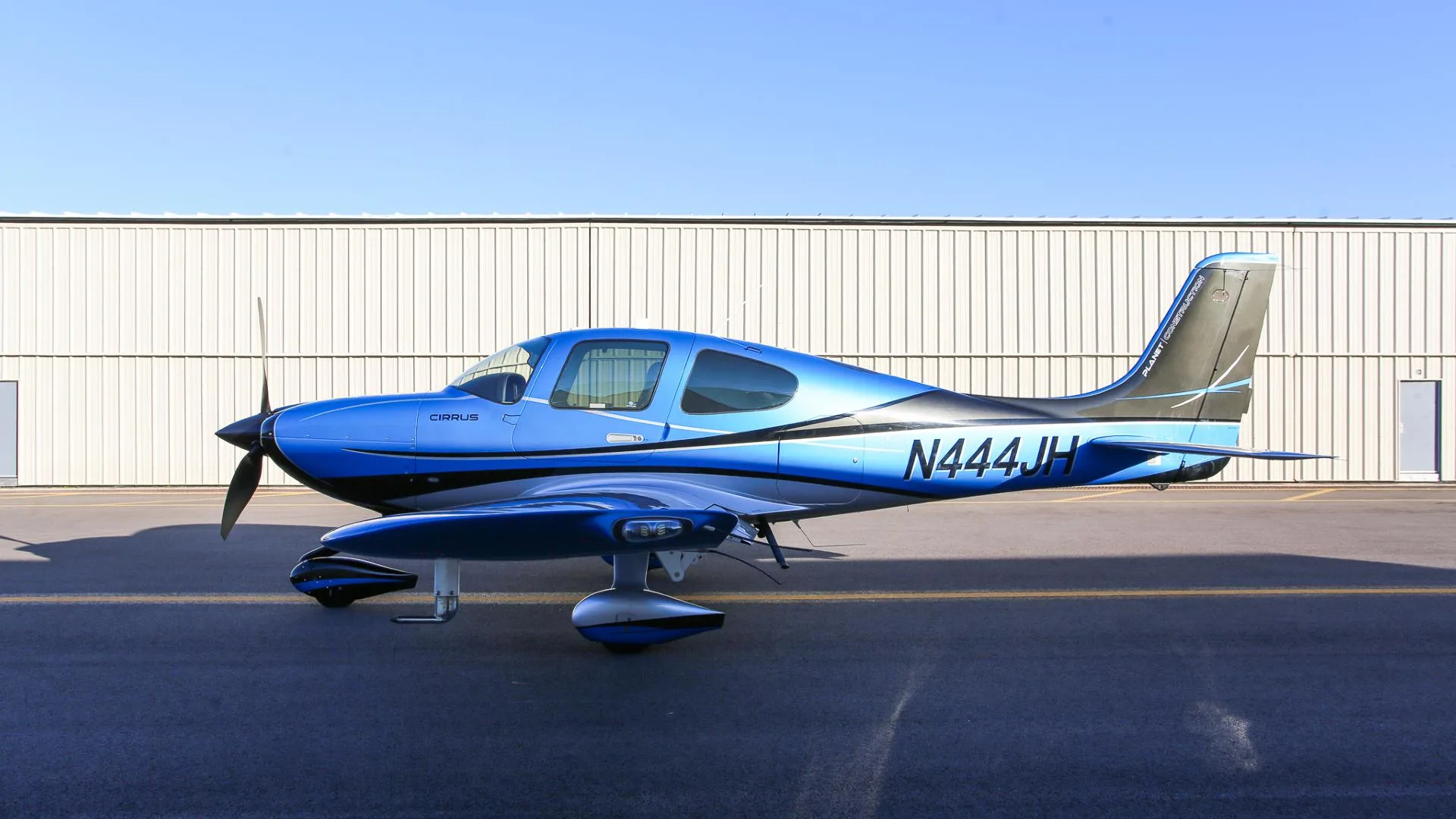 A blue and silver Cirrus SR22 aircraft with registration N444JH parked on a tarmac.