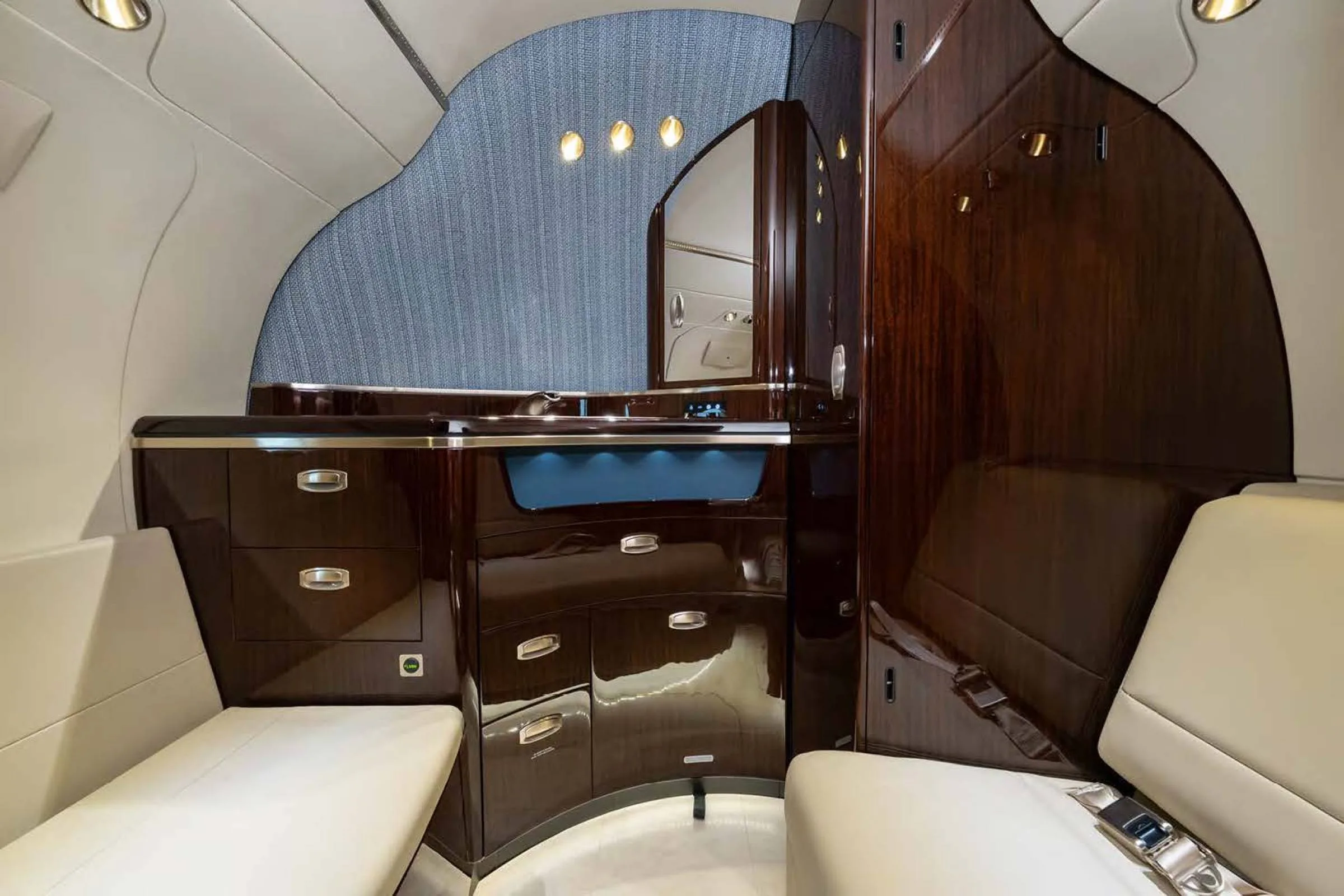The galley or lavatory area of a private jet, featuring dark wood cabinetry, a mirror, and a textured blue wall.
