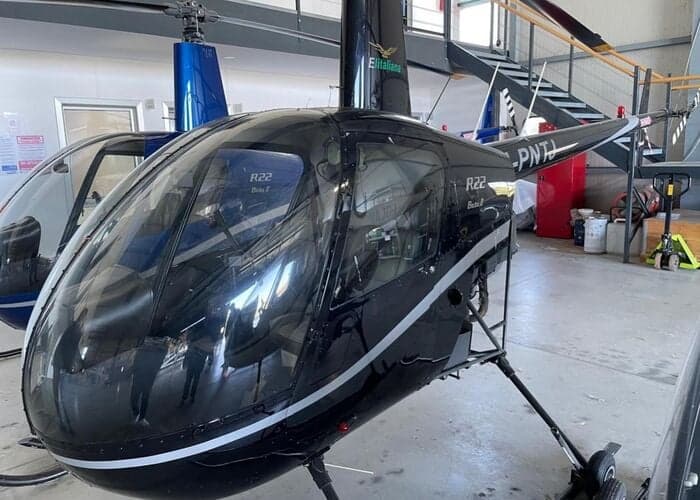 Close-up of a black Robinson R22 Beta II helicopter inside a hangar.