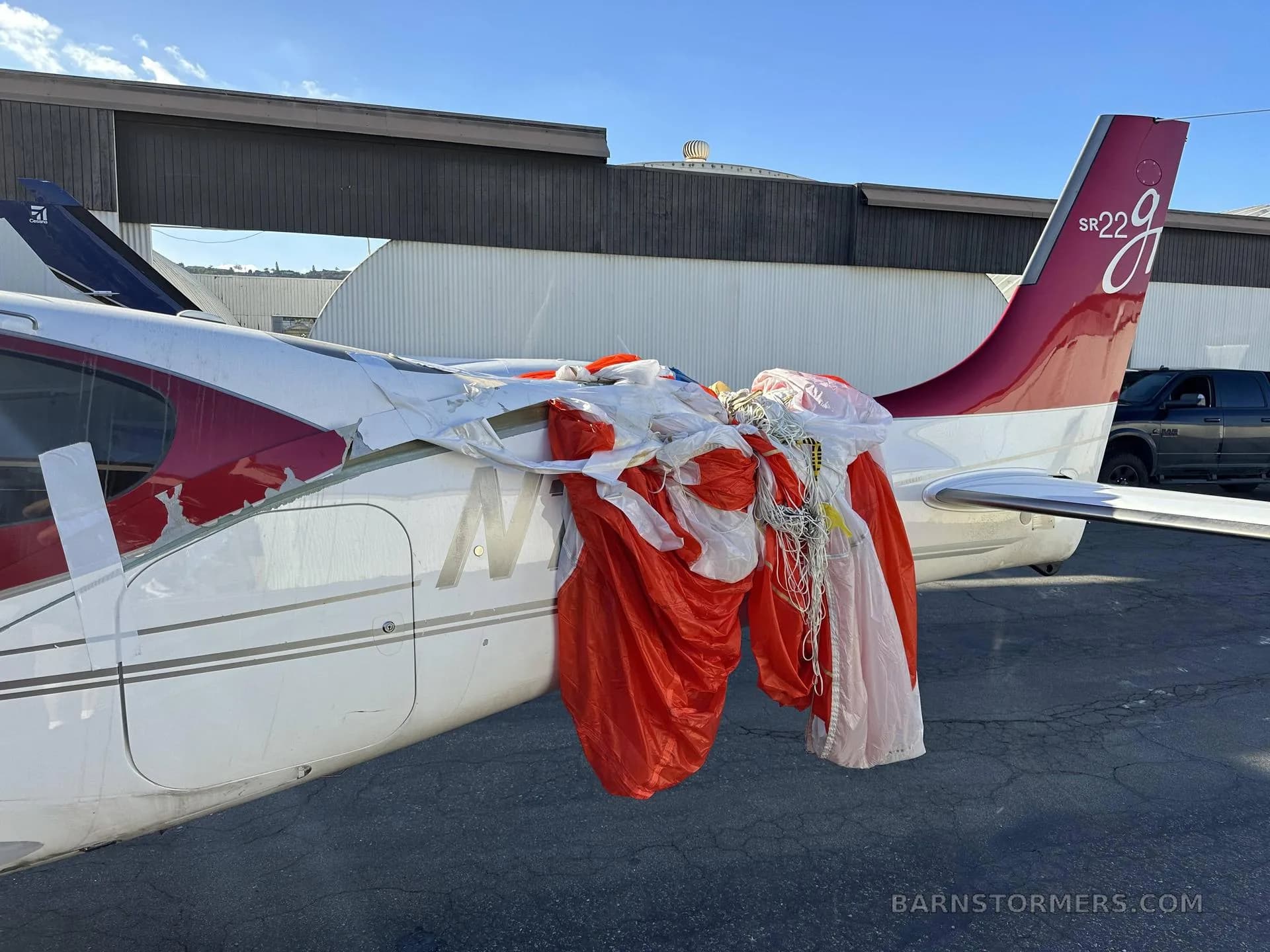 The tail section of a red and white Cirrus SR22 aircraft with its parachute deployed and draped over the rear fuselage.