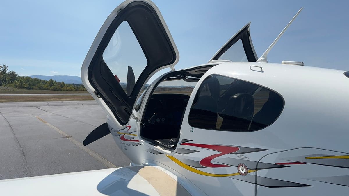 Side view of a Cirrus aircraft with its doors open, showing the cockpit and interior.