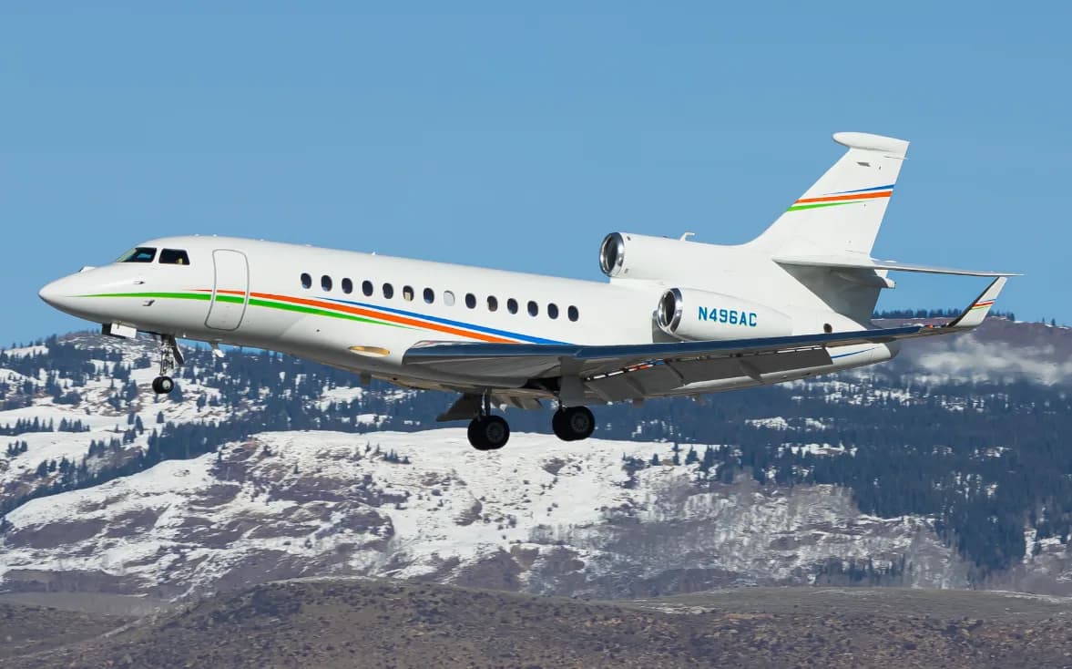 A Falcon 900EX EASy jet in flight over a snowy mountain range.