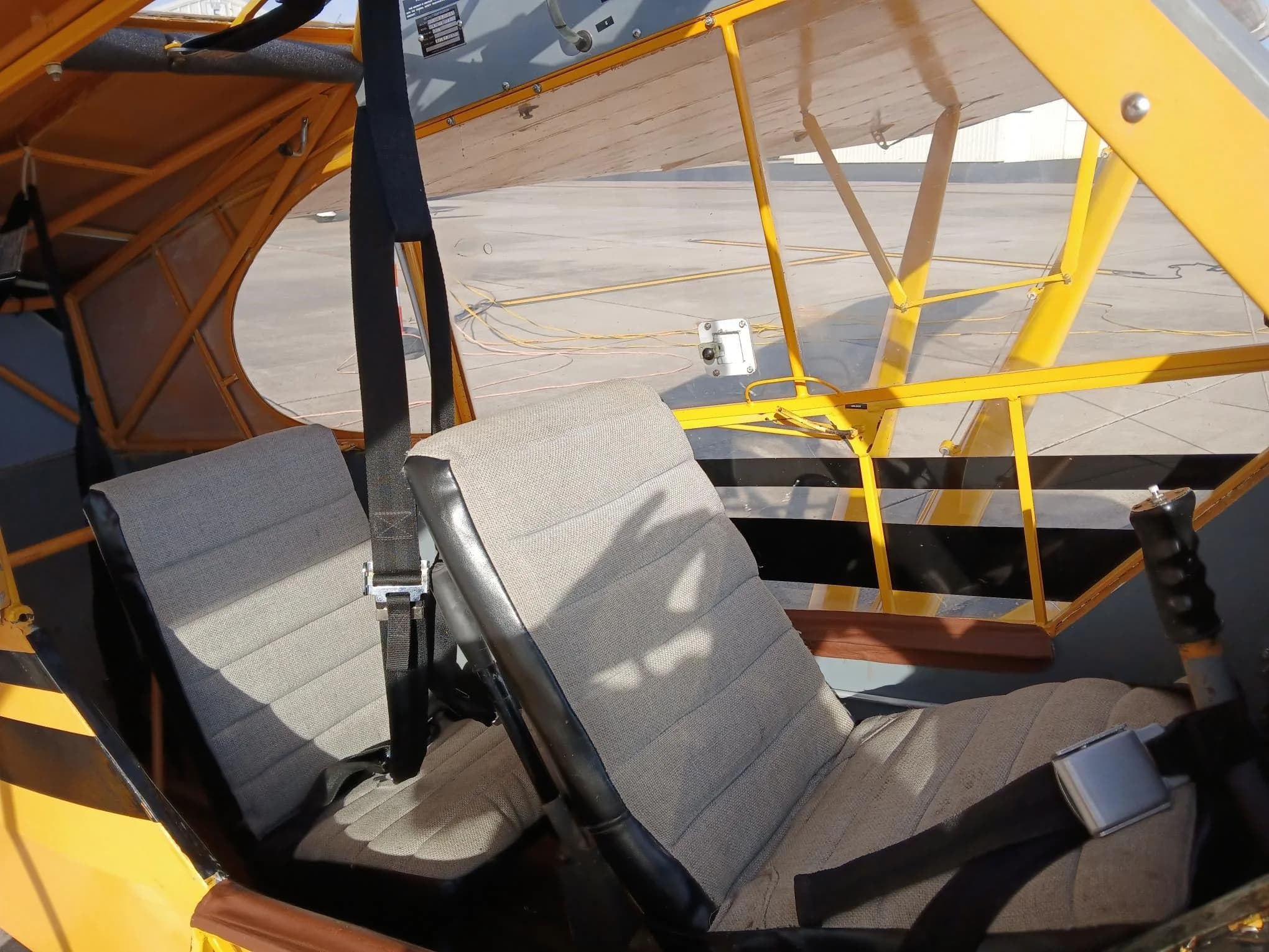 The two fabric seats inside the cockpit of the yellow aircraft, with seatbelts.