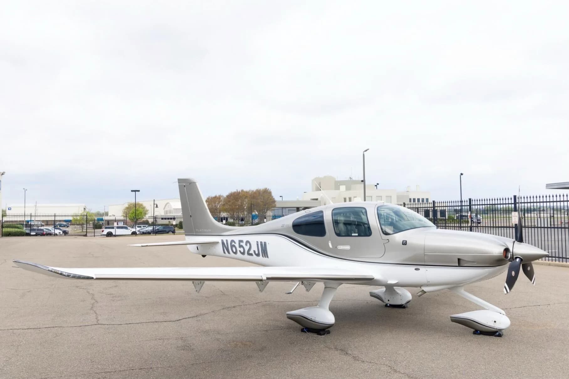 A silver and white Cirrus SR22 aircraft with N652JM registration parked on an airport tarmac with buildings in the background.