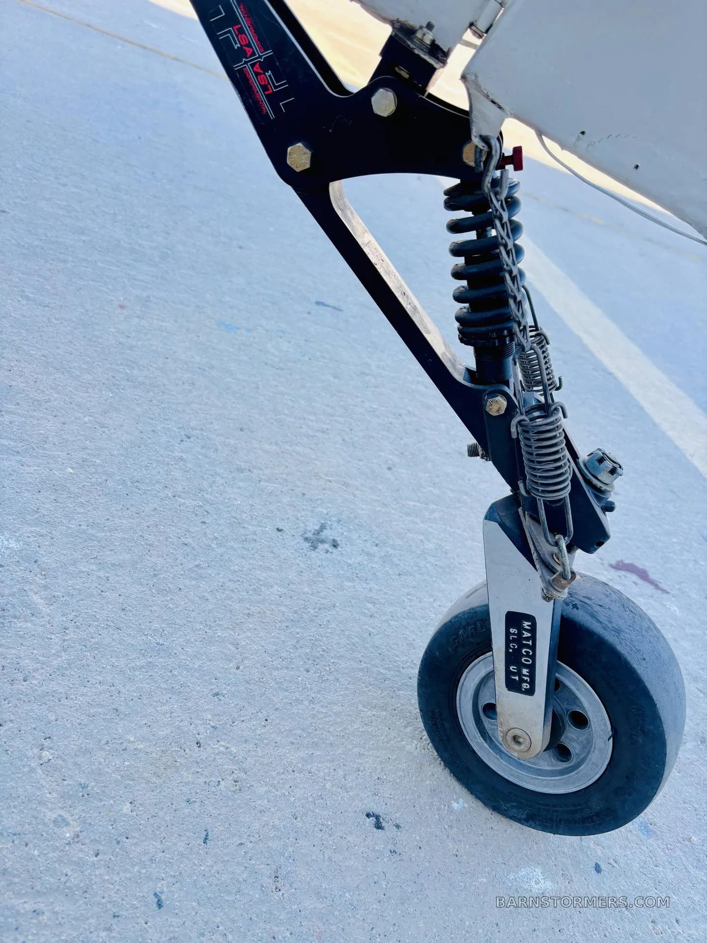 A close-up view of the robust landing gear and tire of an aircraft, showing springs and a "MATCO MFG." label.