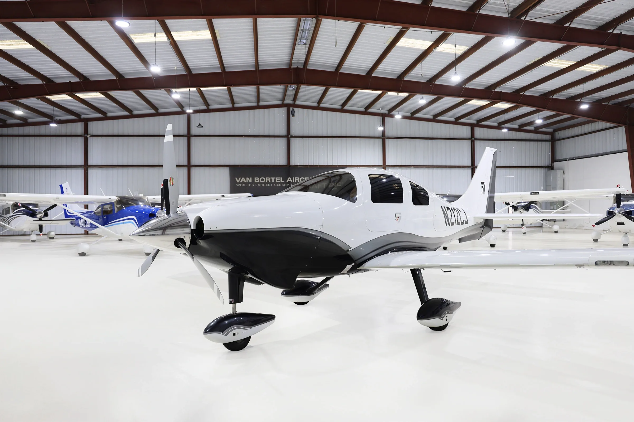A white and black Cessna TTx aircraft (N212CJ) is parked in a hangar, viewed from the front-left.