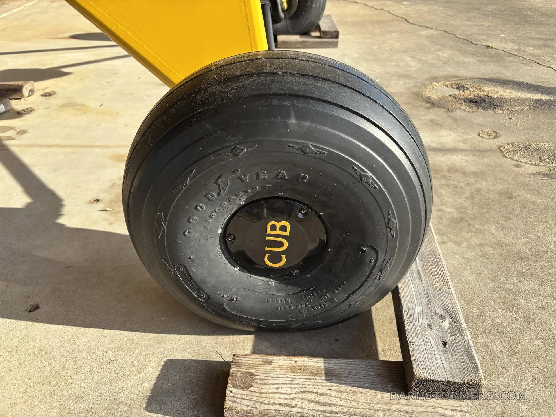 A close-up of a large black Goodyear aircraft tire with 'CUB' on the hubcap, resting on wooden blocks.