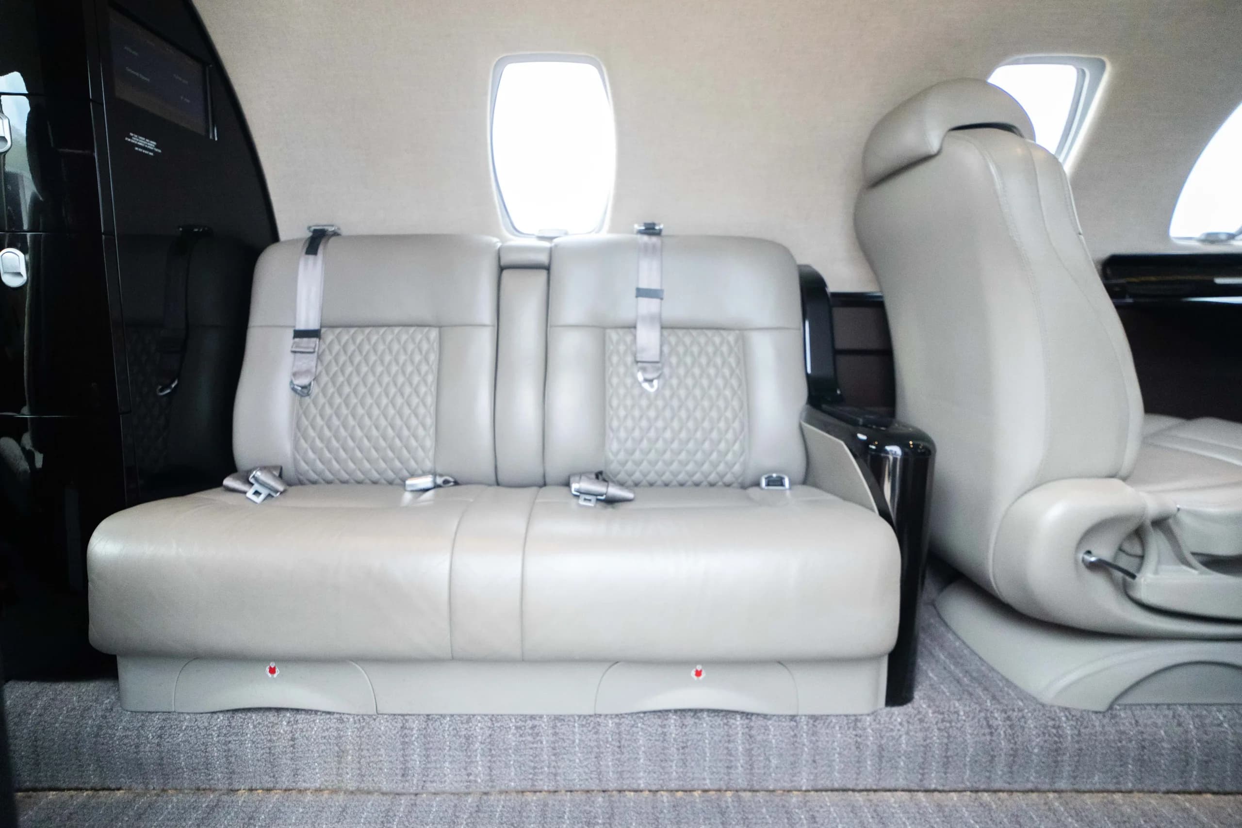 Two light grey leather seats with diamond stitching and seatbelts inside an aircraft cabin.