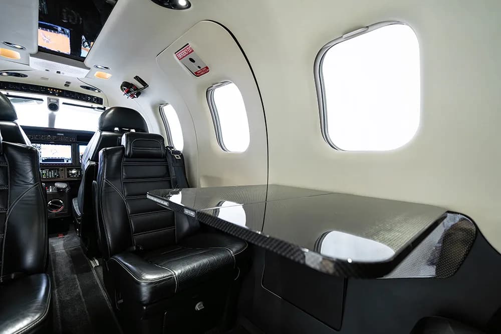 Interior view of the aircraft cabin showing a carbon fiber table and black leather seats.