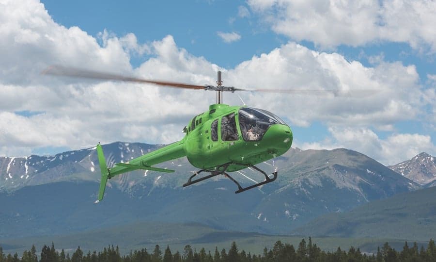 A green helicopter flying in front of a mountain range.