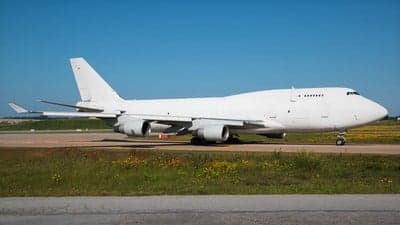 A white Boeing 747 sits on the tarmac on a sunny day.