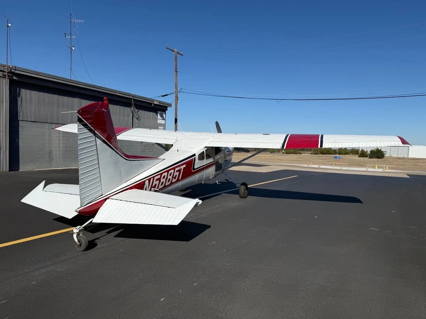 Rear-side view of a white and red single-engine aircraft N5885T parked on an asphalt apron.