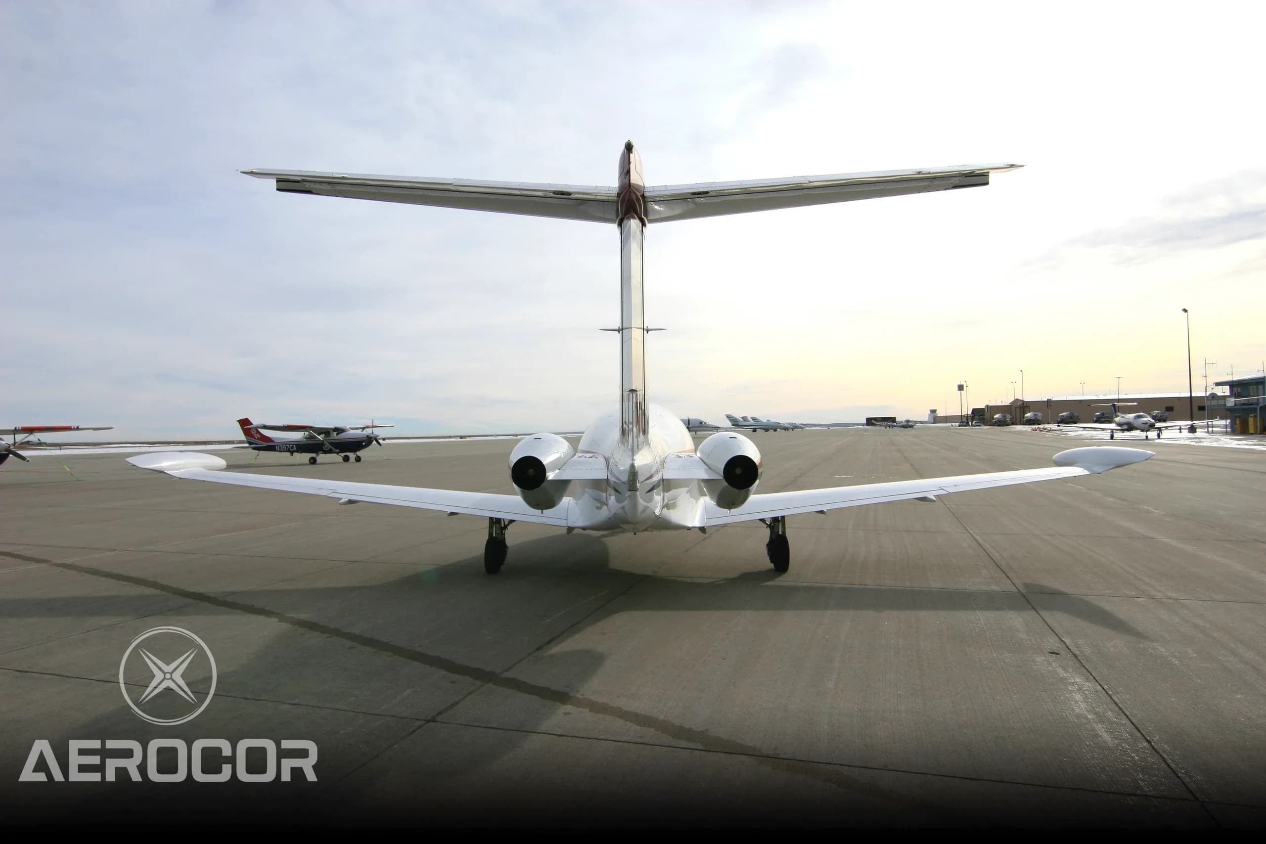 Rear view of a white Eclipse 500 jet with red and blue stripes parked on an airport tarmac at sunset.