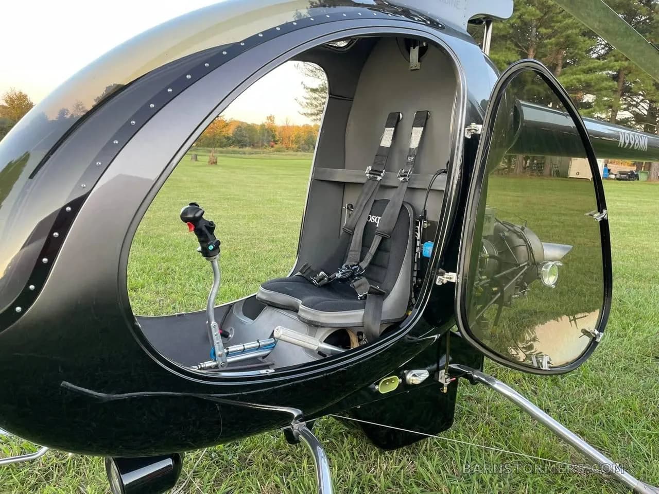 The open cockpit of a black single-seat helicopter shows the seat, controls, and exposed engine in the background.