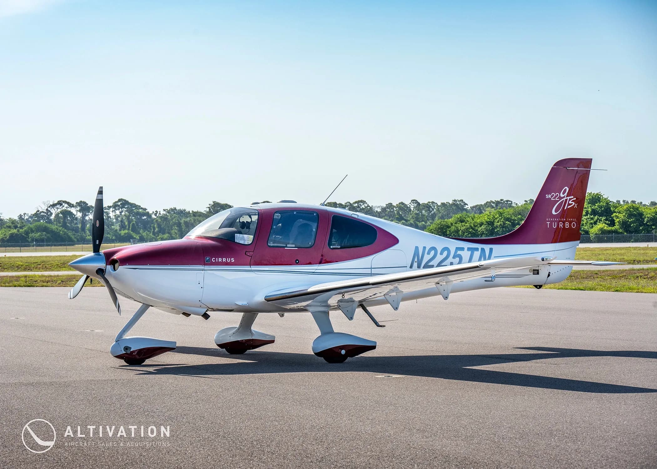 A three-quarter front view of a red and white Cirrus SR22T aircraft (N225TN) parked on an airfield.