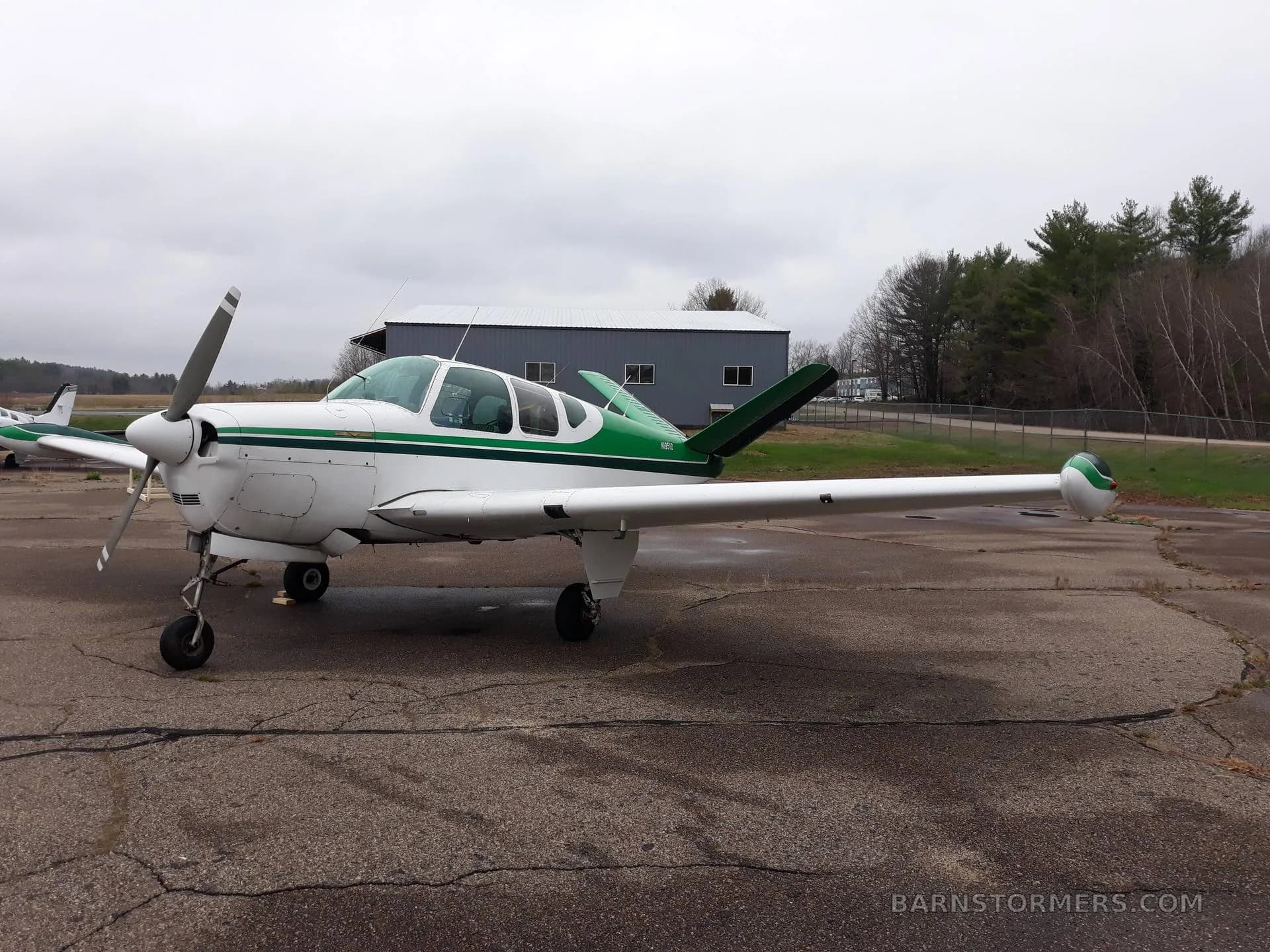 A side view of a white aircraft with green stripes and a V-tail, parked on a cracked tarmac under an overcast sky.