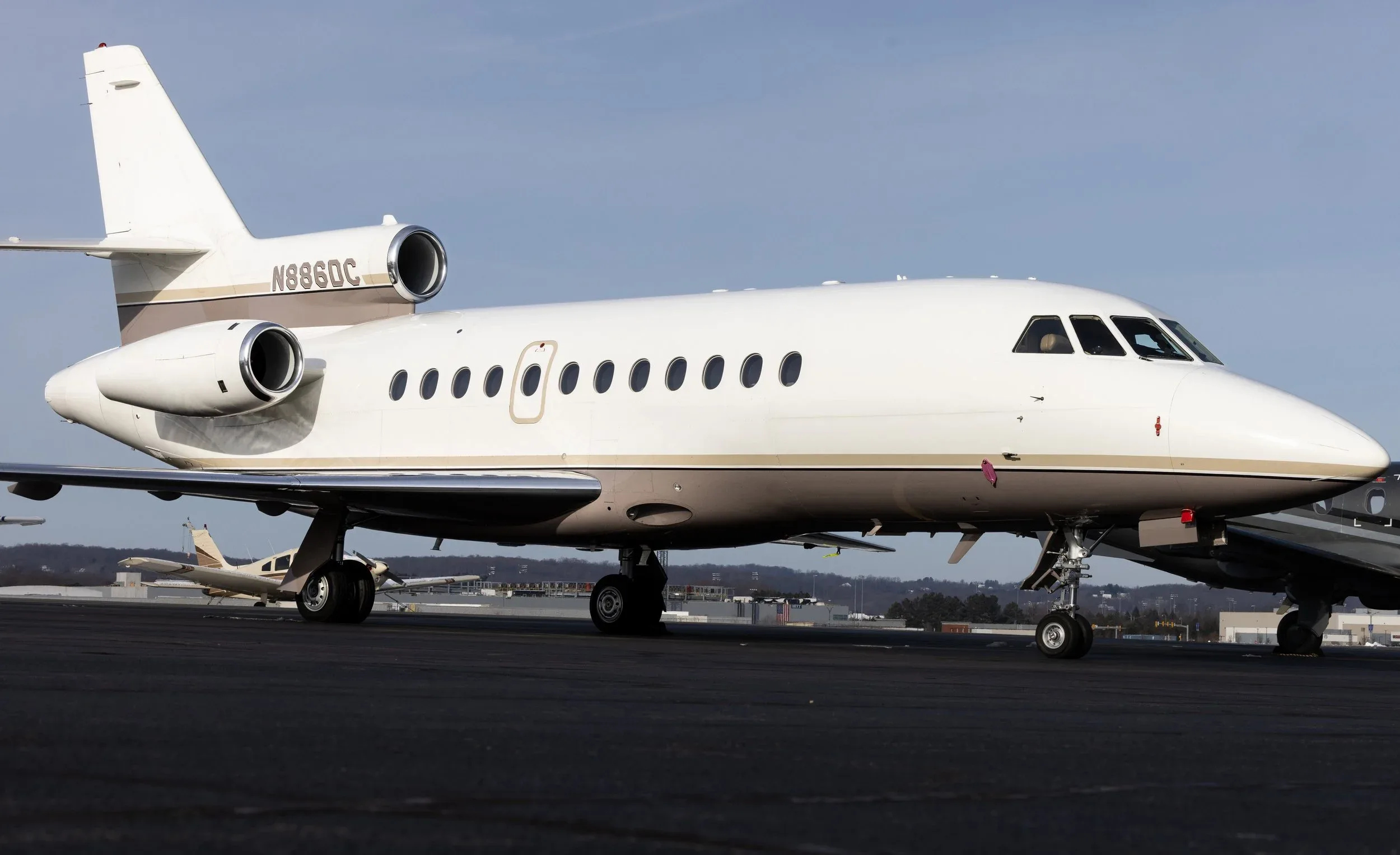 Side view of a white Dassault Falcon 900 aircraft with registration N886DC on the tarmac.