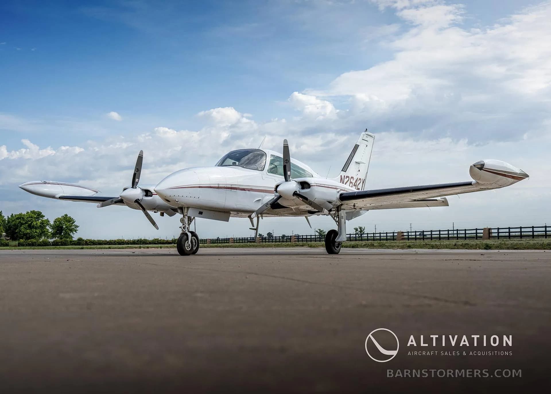 A low-angle front-side view of a white twin-engine propeller aircraft with maroon stripes, registration N2642Y, parked on an asphalt runway.